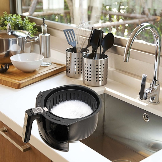 BLACKDECKER AF200 air fryer basket with soap suds in a modern kitchen sink, utensils and cookware in background.