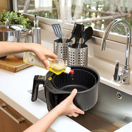 BLACKDECKER AF300 air fryer basket, side angle, person pouring oil inside in modern kitchen.