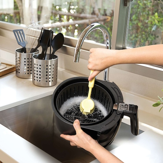 Photo of BLACKDECKER AF300 air fryer basket being hand washed in kitchen sink with soap and brush.