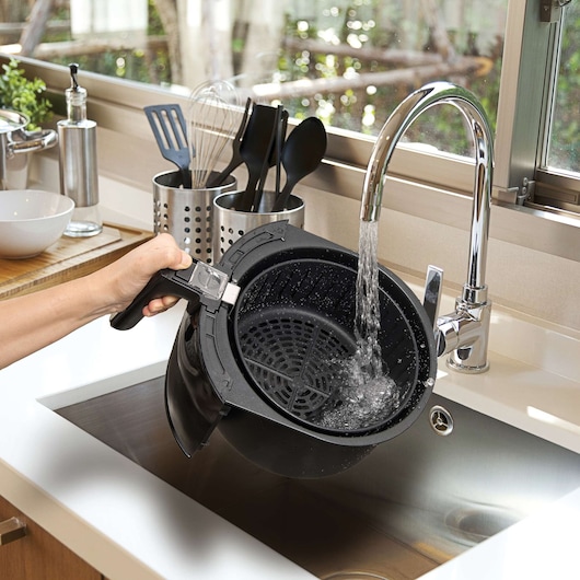 BLACKDECKER AF300 air fryer basket being rinsed under a kitchen faucet, photo in kitchen setting.