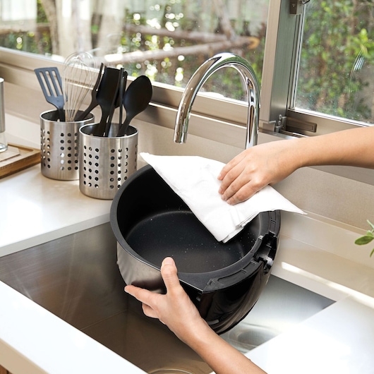 Photo of hands cleaning BLACKDECKER AF400 air fryer basket with a cloth at a kitchen sink.