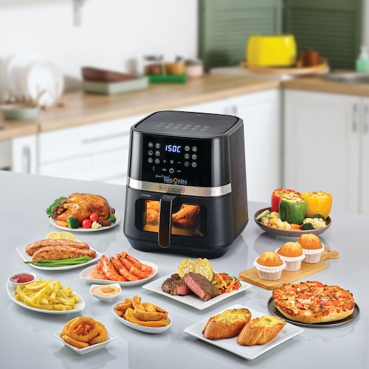 Photo of BLACK+DECKER AF5800 air fryer on kitchen counter surrounded by cooked food dishes including chicken, pizza, steak, fries, shrimp, muffins, and stuffed peppers.