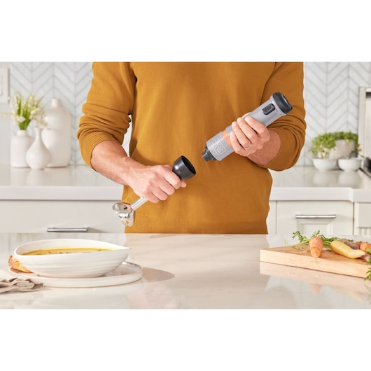 BLACKDECKER BCKM1011KGF hand blender with detachable attachment held in a kitchen setting.