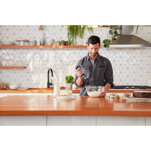 Black+Decker hand mixer BCKM1012KB used in a kitchen, mixing batter in a glass bowl on a wooden counter.