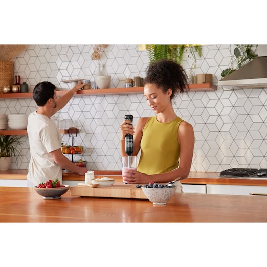 BLACKDECKER BCKM1016KSB hand blender in use blending smoothie in kitchen with fruit bowls on counter.