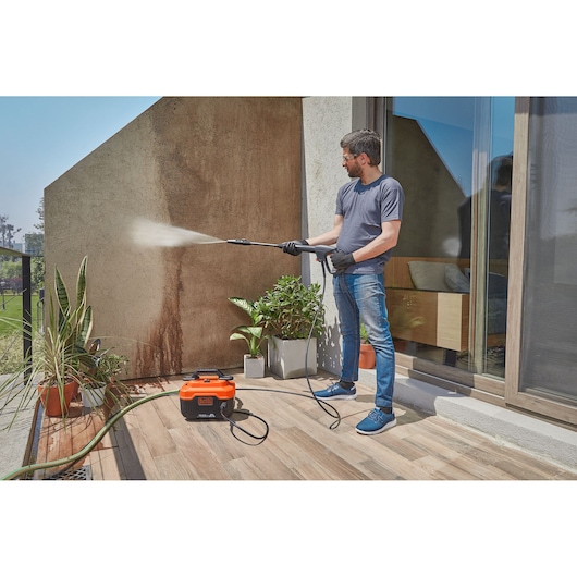 Photo of a person cleaning an outdoor wall with a BLACK+DECKER BEPW1300H pressure washer on a patio.