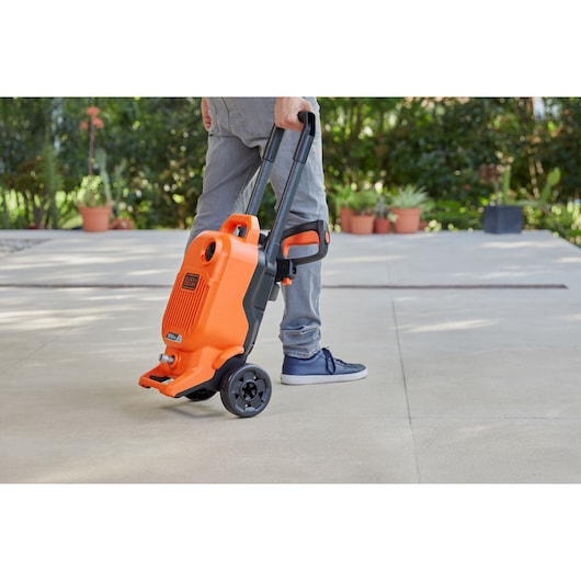 BLACK+DECKER BEPW1700 orange pressure washer with wheels, pulled by a person on outdoor patio.