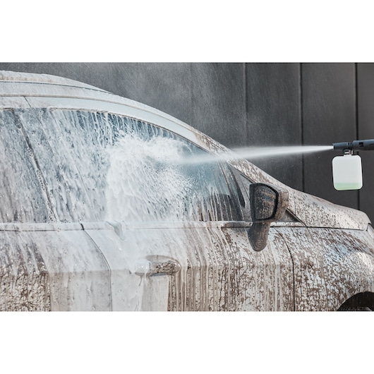 BLACKDECKER BEPW2000 power washer spraying foam on a dirty car, front side view.
