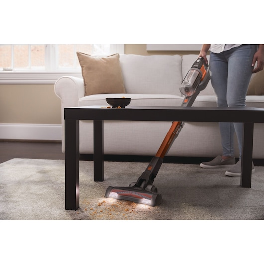 BLACKDECKER BHFEV182C stick vacuum cleaning crumbs under table in living room, carpet visible.