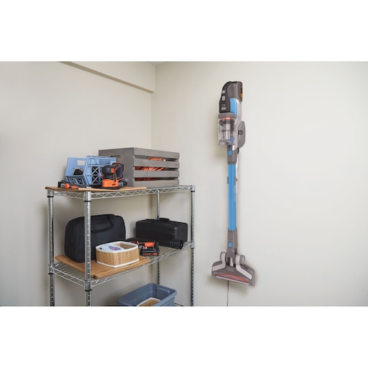 BLACKDECKER BHFEV362D cordless stick vacuum mounted on a wall in a storage room next to metal shelving.