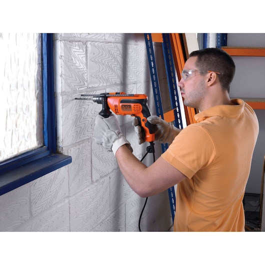 BLACKDECKER CD714REK orange corded drill used for masonry work, held by gloved hands, indoor setting.