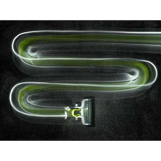 A BLACK+DECKER vacuum cleaner is shown moving in a zigzag pattern on a dark surface, with a light trail effect highlighting its cleaning movement.