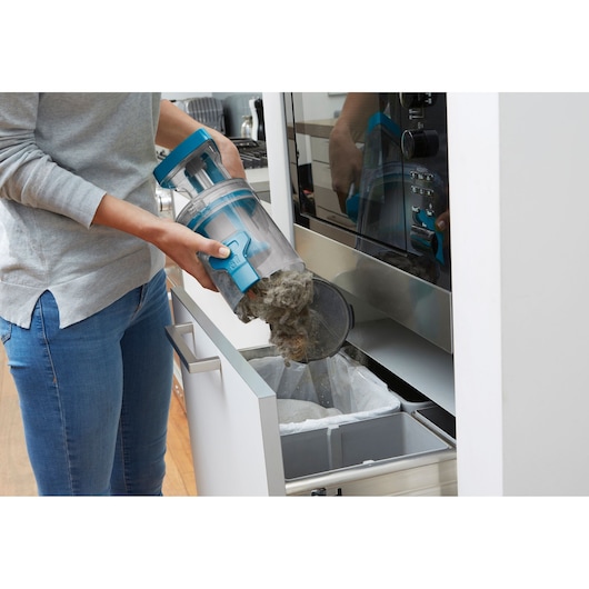 BLACKDECKER CUA525BH vacuum container being emptied into a trash bin in a kitchen scene, side angle.