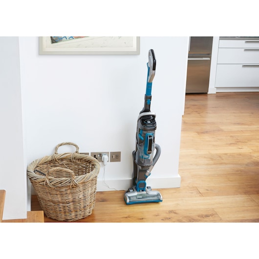 BLACKDECKER CUA525BH upright vacuum cleaner with blue accents on wooden floor beside wicker basket.