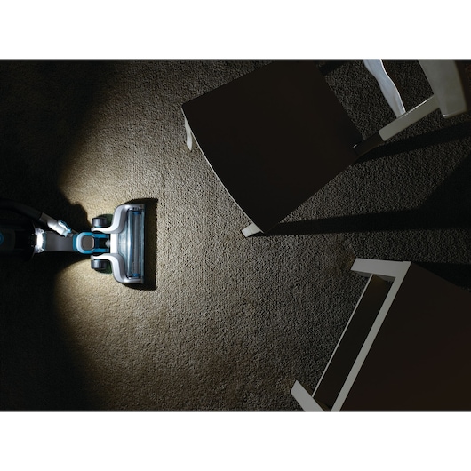 BLACKDECKER CUA525BH vacuum cleaner head with LED light cleaning carpet under chairs, top view.