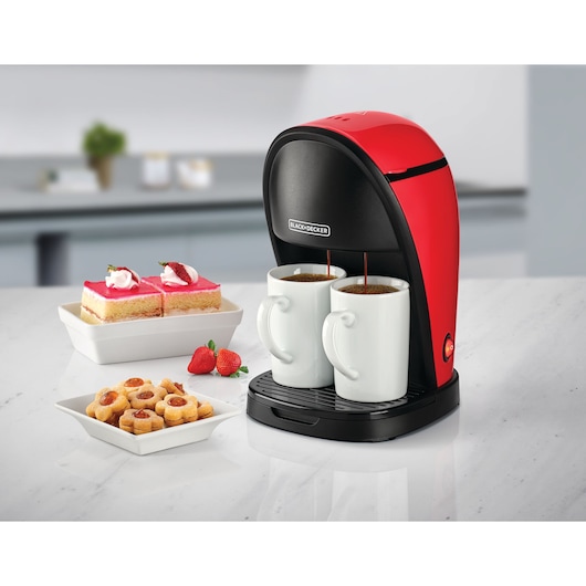 BLACK+DECKER DCM48 red and black coffee maker brewing two cups, desserts and strawberries on kitchen counter.