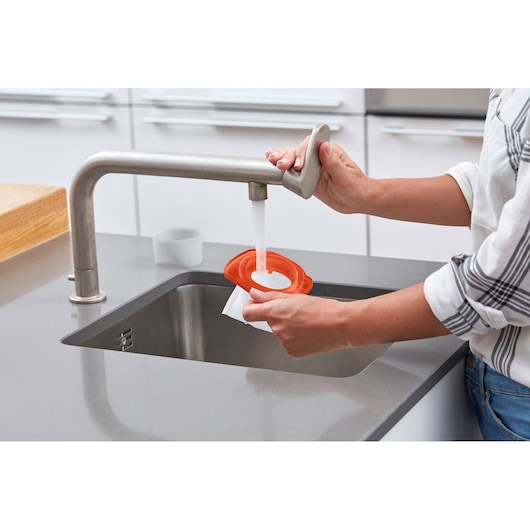 BLACKDECKER DVB315JP vacuum filter being rinsed under kitchen faucet, close-up angle.