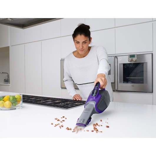 BLACKDECKER DVJ325BFSP handheld vacuum cleaning crumbs on kitchen counter, purple and gray design.