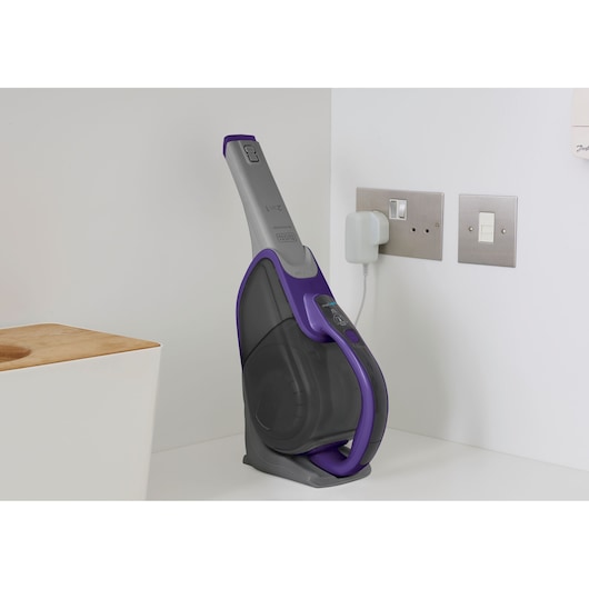 BLACKDECKER DVJ325BFSP cordless handheld vacuum in charging dock, grey and purple, on countertop.