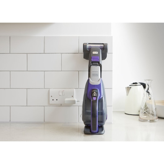 BLACKDECKER DVJ325BFSP handheld vacuum in purple, front angle, charging on kitchen counter.