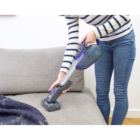 BLACKDECKER DVJ325BFSP handheld vacuum cleaning a gray sofa in a home setting.