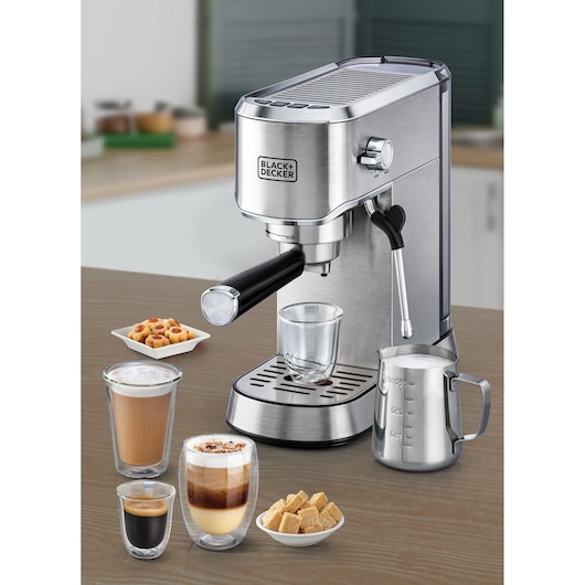 BLACK+DECKER ECM150 espresso machine on a counter with glass cups, milk frothing pitcher, sugar cubes, and cookies.