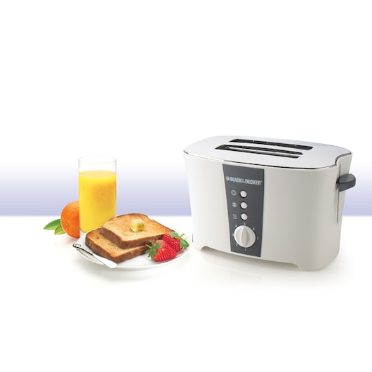 A BLACK+DECKER two-slice toaster (model ET122) in white and grey is shown with a breakfast setup including a plate of buttered toast, strawberries, an orange, and a glass of orange juice.