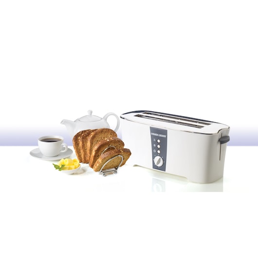 A BLACK+DECKER long slot toaster model ET124 is shown next to a white teapot, a cup of coffee, slices of bread on a rack, and a small plate with butter and mint leaves. The setup is on a white surface and background.