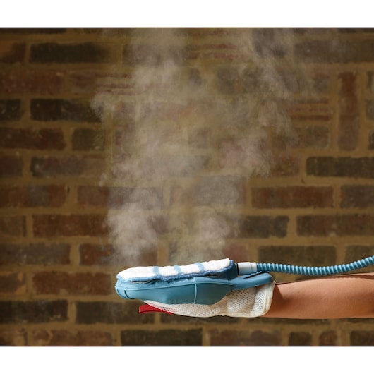 BLACKDECKER steam cleaning glove FSH10SM with visible steam, worn on hand against brick wall background.