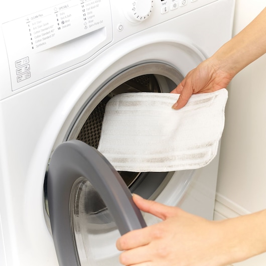 BLACKDECKER FSM1605 microfiber pad being placed in a washing machine, close-up angle.