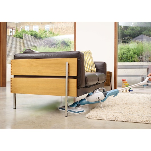 BLACKDECKER FSMH13151SM steam mop cleaning under brown sofa on polished floor near white rug.
