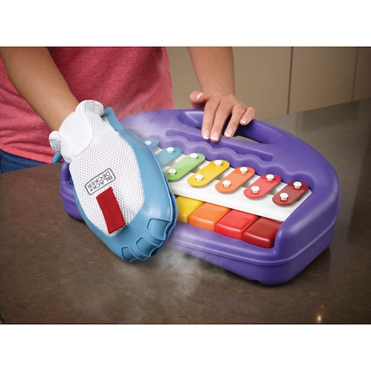 BLACKDECKER FSMH13151SM steam glove cleaning a purple toy xylophone on a countertop, side angle.