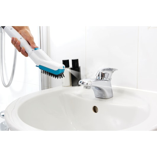 BLACK+DECKER FSMH13151SM steam cleaner used on bathroom sink faucet, photography showing cleaning action.