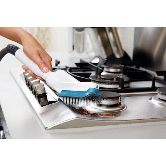 BLACKDECKER FSMH13151SM steam cleaner with brush accessory cleaning a stainless steel gas stove top.