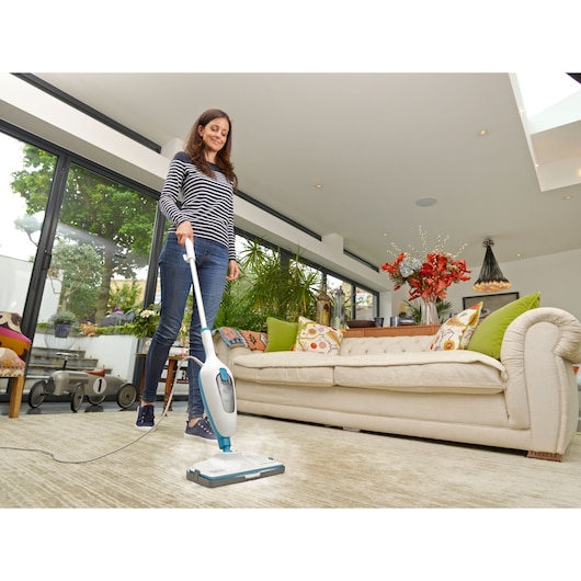 BLACK+DECKER FSMH13E10 steam mop being used on a light carpet in a modern living room with a beige sofa.