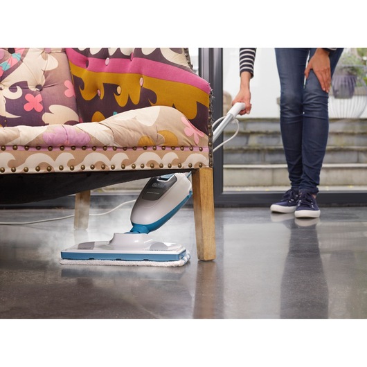 BLACKDECKER FSMH13E10 steam mop cleaning dark floor under colorful chair, handled by person.