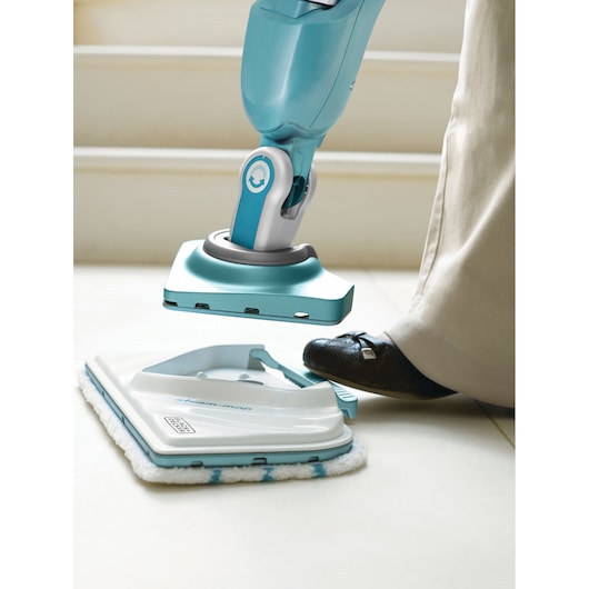 BLACK+DECKER steam mop FSMP30 being detached from cleaning pad on tile floor, close-up view.