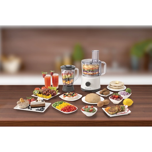 BLACKDECKER FX822 food processor and blender on table with assorted fruits, vegetables, drinks, and prepared dishes.