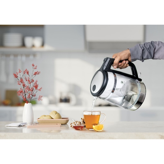 BLACKDECKER GK220 electric kettle pouring hot water into a glass cup on a kitchen counter.