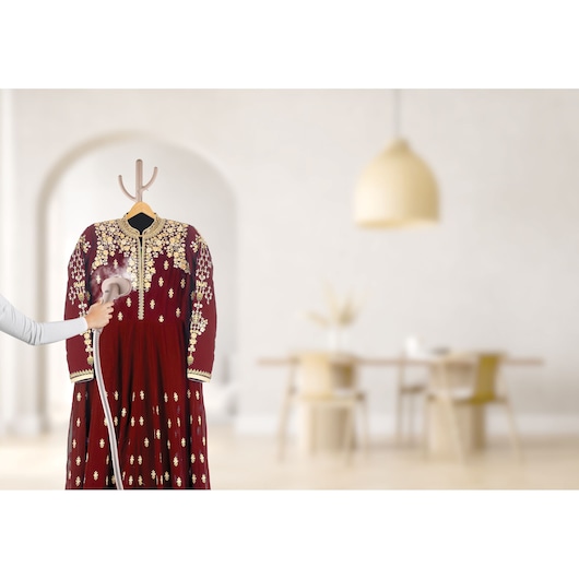 BLACKDECKER GST1620 handheld garment steamer in use on a red embellished dress, home setting in background.