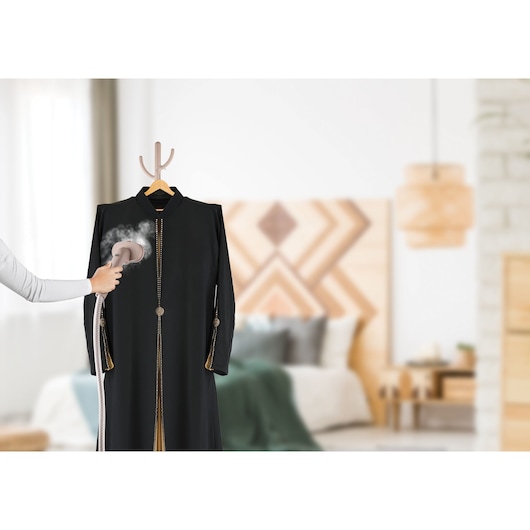 BLACKDECKER GST1620 handheld garment steamer releasing steam onto a black robe in a bedroom setting.