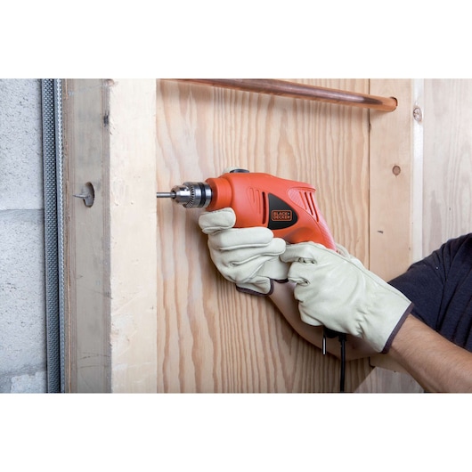 Photo of BLACKDECKER HD5010 orange corded drill used on wooden panel, person wearing work gloves.
