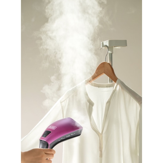 BLACKDECKER HSTD1600 handheld garment steamer in purple used to steam a white shirt on hanger, front view.