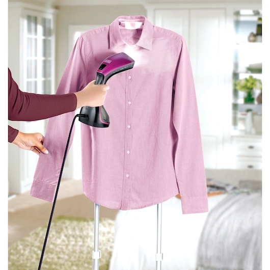 BLACKDECKER HSTD1600 handheld garment steamer in use on a pink shirt in a bedroom setting.