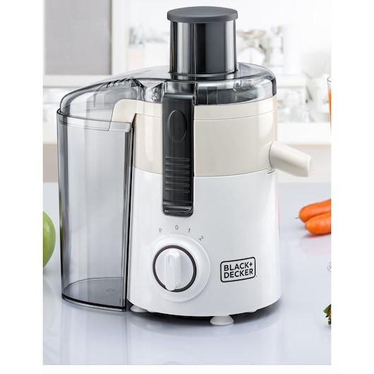 A BLACK+DECKER electric juicer with a white and transparent design is shown on a kitchen counter. The appliance features a control dial with settings labeled P, 0, 1, and 2, and a spout for pouring juice. There are fresh fruits and vegetables, including apples and carrots, visible around the juicer.