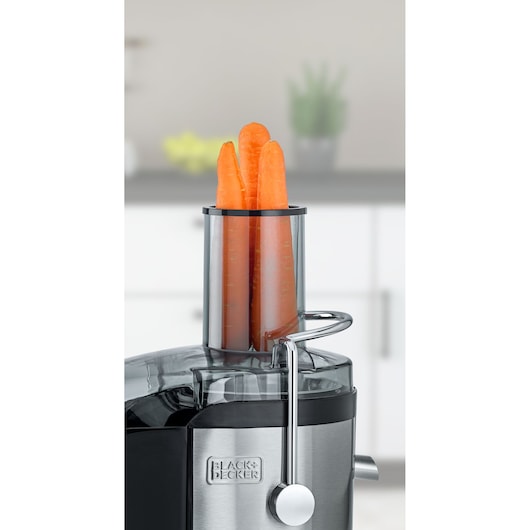 BLACKDECKER JE800 juicer with carrots in feed chute, close-up on stainless steel body, kitchen background.