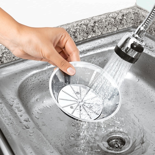 BLACKDECKER JE800 juicer mesh filter being rinsed under running water in a kitchen sink, close-up.