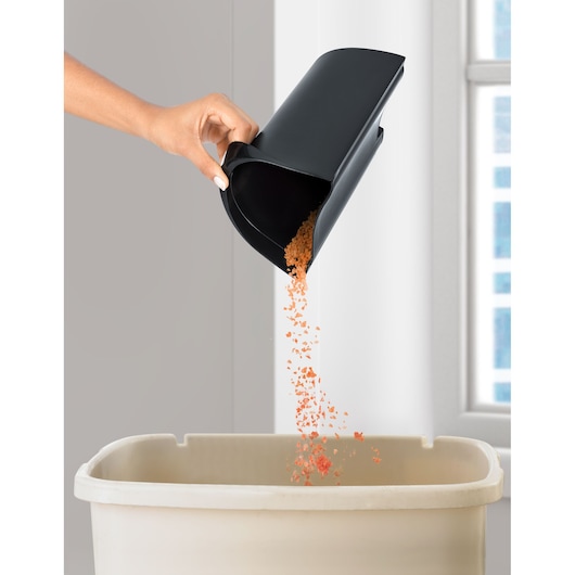 BLACKDECKER JE800 juicer pulp container being emptied by hand into a beige bin, close-up indoor view.