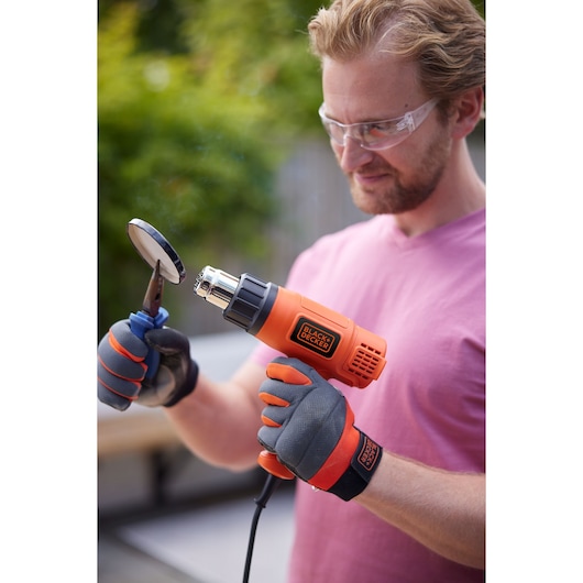Photo of BLACK+DECKER KX1650 heat gun being used outdoors by a person wearing protective gloves.