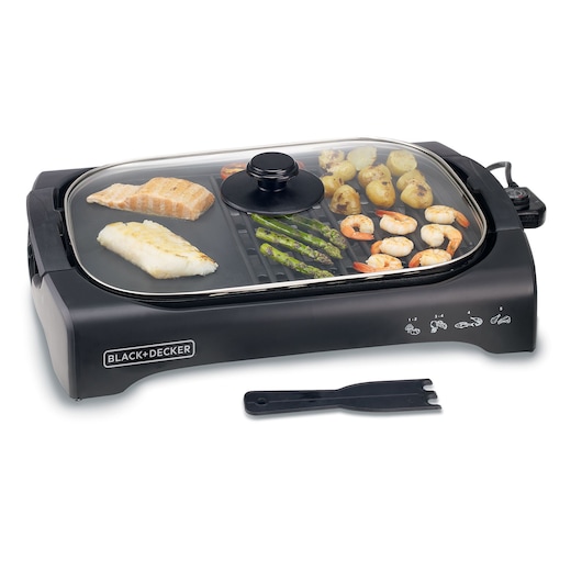 A BLACK+DECKER electric grill with a glass lid, grilling fish, shrimp, asparagus, potatoes, and cherry tomatoes. A plastic spatula tool is placed in front of the grill.